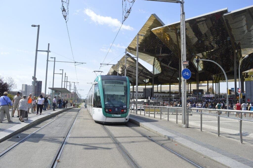 A tram waiting at a stop beside a large angular canopy in Barcelona
